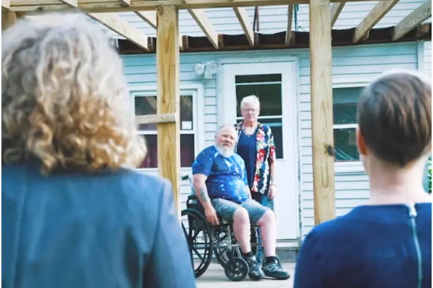 Man in a wheelchair outside his home with family members