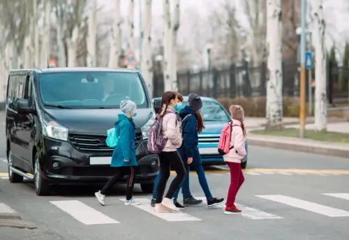 School children cross the road in medical masks. Children go to school.
